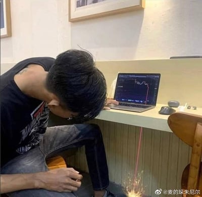 图中一名男子低着头，将脸埋在膝盖附近，看起来十分沮丧崩溃。面前的笔记本电脑屏幕显示着暴跌的股票K线走势图，通过视觉错位的P图手法，把K线图上的下跌红线延伸到地面的火花处，仿佛暴跌的走势“击穿”桌面，直接“扎”到了男子的位置，用极具创意的视觉效果，生动调侃了股民在股票暴跌、投资亏损后的绝望心态。