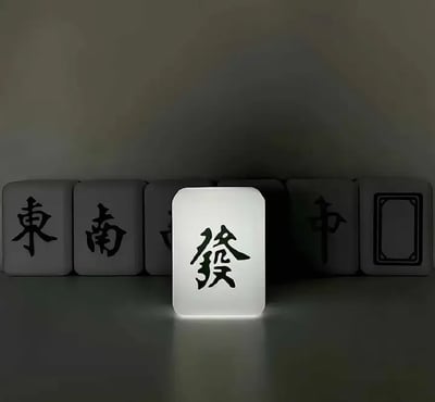 图片展示了一排麻将牌，其中“发财”牌被特别点亮，处于中央C位，显得格外突出。背景其他麻将牌相对黯淡，包括东、南、中等。形象地表现了“发财”在麻将以及现实中的吸引力和重要性，有“C位出道”之意，也有‘发财光环加持’的双关梗，暗示大家都关注发大财。适合用来表达对财富的渴望，或在需要‘好运’、‘吸财’、‘站C位’的语境下使用。