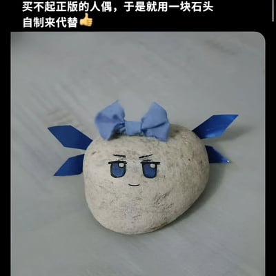 图片展示了一个创意DIY作品：一块普通的石头被改造成简易人偶。石头上用蓝色颜料绘制了卡通风格的眼睛、眉毛和嘴巴，表情看起来有些严肃。石头顶部装饰着一个蓝色的纸质蝴蝶结，两侧各有两个蓝色的纸质装饰，类似翅膀或飘带。图片上方配有文字说明：'买不起正版的人偶，于是就用一块石头自制来代替👍'，表达了用低成本创意替代昂贵正版商品的幽默态度。