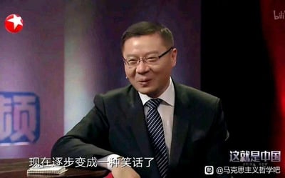 图片为《这就是中国》节目截图，主持人张维为身穿黑色西装，佩戴眼镜，坐在桌前，面带微笑。背景有东方卫视红色五角星台标，右下角显示节目名称“这就是中国”。画面底部有白色字幕“现在逐步变成一种笑话了”，右上角有bilibili平台标识，右下角有水印“帖 @马克思主义哲学吧”。