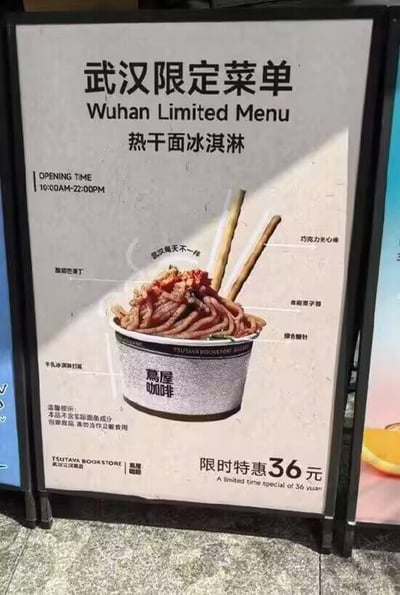 这是茑屋咖啡武汉江汉路店推出的限定款产品宣传立牌，整体为浅米色背景，主体是装在印有茑屋咖啡标识的纸碗里的热干面造型冰淇淋实拍图，各个配料都有标注线说明：底层为牛乳冰淇淋打底，表面是做成面条形态的熔岩栗子蓉，搭配酸甜芒果丁、绿色糖针，顶部插有两根巧克力夹心棒，还原热干面的外观；立牌顶部是“武汉限定菜单 热干面冰淇淋”的中英文标题，左侧标注门店营业时间为10:00到22:00，底部标注了温馨提示，说明该产品不含真实面条成分，属于创意甜品不可作为正餐食用，同时标注了出品方信息与限时特惠36元的售价，是结合武汉本土特色美食热干面打造的跨界创意甜品宣传物料。