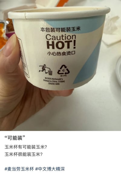 这张图文混排的图片上半部分为实拍内容：一只手举着麦当劳的玉米纸容器，杯身印刷有“本包装可能装玉米”“Caution HOT! 小心热食烫口”的提示文字，还有垃圾投放提示、回收标识以及麦当劳2025年版权标识。图片下半部分是配文玩梗，利用“可能”的中文歧义，给出两种完全不同的解读：一是玉米杯有可能装了玉米，二是玉米杯的容量很能装玉米，最后带有#麦当劳玉米杯、#中文博大精深的话题标签，调侃中文语义的多样性带来的趣味效果。