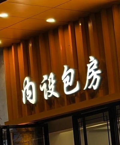 这是一张实地拍摄的线下餐饮店铺门头照片，画面展示了店铺入口上方的区域：棕色竖条状的装饰墙面上，安装着白色的立体发光字招牌，文字内容为“内设包房”，上方天花板还有嵌入式的圆形顶灯，灯光亮起。该招牌用于告知到店顾客，此店铺内设有可供使用的包房空间，适合有私密用餐需求的顾客选择，图中文字没有双关、谐音梗等特殊含义。