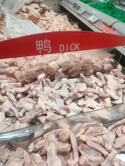 这是超市冷冻货区的实拍场景，货柜里摆放着大量冷冻鸭翅根等鸭类分割肉制品，上方的红色价签将中文“鸭”错误翻译成英文单词“DICK”。
该翻译是核心笑点：“DICK”在英文中是粗俗俚语，指代男性生殖器，和“鸭（鸭肉）”的正确英文表述完全不符，属于翻译失误造成的尴尬又搞笑的场景。