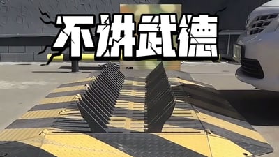 图片展示了一个停车场场景，地面上有一排竖起的黑色尖刺路障，路障底部有黄黑相间的警示条纹。画面右侧可见一辆白色汽车的前部，似乎正要接近路障。图片顶部有醒目的白色大字“不讲武德”，字体带有裂纹效果，增强视觉冲击力。该图通过将“不讲武德”这一网络梗与具有攻击性的路障结合，调侃这种突然出现的障碍物如同“不按套路出牌”的行为，带有幽默和戏谑的意味。