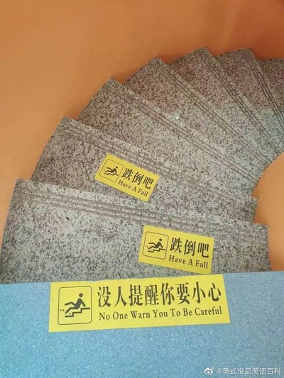 这是一张拍摄室内楼梯的图片，楼梯的花岗岩台阶上贴了三张黄色警示贴纸：前两张将常规的“小心跌倒”恶搞成“跌倒吧 Have A Fall”，搭配标准的摔倒警示图标；最下方的贴纸更是玩梗升级，写成“没人提醒你要小心 No One Warn You To Be Careful”。原本用于提醒安全的标语被反向恶搞，用错误翻译和反差感制造出荒诞搞笑的效果，打破了人们对安全警示的常规认知。