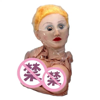 图片中展示了一个金发人偶头部，面部表情略显诡异，眼睛瞪得很大，嘴唇涂着鲜艳的红色。人偶头部被透明塑料覆盖，胸前位置叠加了两个粉红色的禁止标识，上面都有“禁”字。整体画面给人一种怪异又略带幽默的感觉。