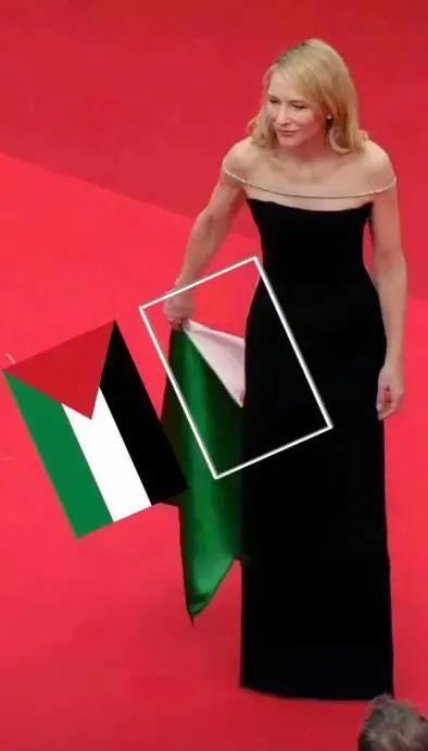 图片中一位身着黑色露肩长裙的女性站在红色地毯上，面带微笑。她的右手似乎正拿着一面绿色和白色的旗帜。图片经过编辑处理，在她手中的旗帜旁添加了一个巴勒斯坦国旗的图示，并通过白色方框和箭头进行标注，暗示她手中的旗帜与巴勒斯坦国旗有关联。