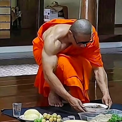 这张图片拍摄了一位身穿橙色僧袍的僧侣正在寺庙地板上吃饭。他的手臂肌肉非常发达，和传统印象中的僧侣形象形成强烈反差，给人一种力量型和尚的幽默感。图片下方出现了各种食物和餐具，场面十分日常，却因为僧侣健身般的身材而显得戏剧感十足。

该梗图特点主要是“僧侣气质”和“健美身材”的反差，容易被网友用来吐槽吃饭、健身、精神与肉体的对比等场景。没有明显的双关或谐音梗，但“健壮和尚”本身具备强烈的视觉和语义冲击力，常被调侃为“力量僧”、“练武僧”。