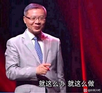 这张图是学者张维为的公开演讲视频截图，他身着浅灰色西装搭配蓝色带花纹领带，戴着眼镜，面带微笑，右手食指指向前方，神态语气笃定。图片下方被添加了白色文字“就这么办 就这么做”，赋予了截图干脆拍板、下定决心的情绪，常被用作网络社交中表达敲定方案、坚定执行态度的表情包，图中没有双关、谐音梗或暗示内容。