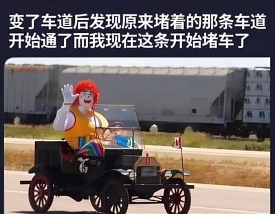 图片上方有一行文字："变了车道后发现原来堵着的那条车道开始通了而我现在这条开始堵车了"。图片主体是一个戴着红色假发、穿着黄色背心的小丑坐在一辆老式黑色汽车里向镜头挥手，车身上插着一面加拿大小国旗。背景中可以看到高速公路和集装箱卡车。这张图片用小丑挥手的欢快形象与文字描述的令人沮丧的驾驶经历形成对比，幽默地表达了司机在变道后发现原车道变得通畅的无奈感受。