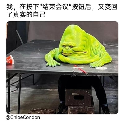 这张梗图通过一个趴在桌面上的绿色萎靡怪物道具，搭配桌子下方的真人支撑的视觉错位形式，结合顶部文字“我，在按下'结束会议'按钮后，又变回了真实的自己”，精准刻画了职场人在经历线上会议后，从需要维持的状态瞬间切换到疲惫、萎靡的真实状态的反差感，夸张地放大了职场人长时间参会后的身心俱疲，引发广大职场人的共鸣。
