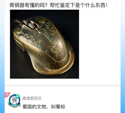 这是一张社交媒体互动截图，上方是用户发布的提问：“青铜器有懂的吗？帮忙鉴定下是个什么东西！”，并附上一张被做旧成青铜器质感、表面带有仿古纹饰的电脑鼠标图片，将现代鼠标伪装成古青铜器提问；下方用户“鹿堡肥鸡贝”回复：“蜀国的文物，叫蜀标”，玩了“鼠标”谐音“蜀标”的双关梗，通过谐音的方式调侃这个仿青铜器外观的鼠标，制造出荒诞搞笑的互动效果。