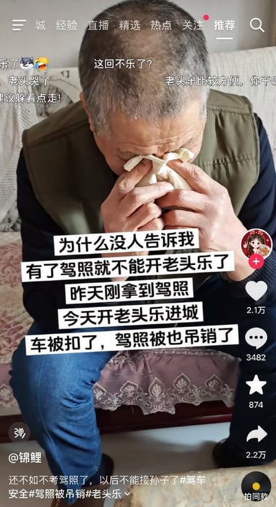 一位头发花白的大爷坐在沙发上，用纸巾捂着脸，表情悲伤。图片配文显示他刚拿到驾照，结果开老头乐（低速电动车）进城时车被扣、驾照也被吊销，配文'为什么没人告诉我有了驾照就不能开老头乐了'。周围还有网友调侃评论'这回不乐了？''老头乐比较方便，你干嘛'等，整体呈现一种因不了解交通规则而遭遇窘境的无奈又略带搞笑的场景。