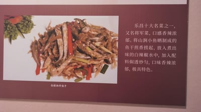 这是一张介绍粤北乐昌特色名菜的图文展示图，左侧是**白辣椒炒鱼干**的菜品实拍：由山涧小鱼晒制的鱼干，搭配白辣椒、红辣椒段与葱段一同烹制，色泽油亮浓郁，摆盘精致；右侧是菜品的详细文字介绍，说明它是「乐昌十大名菜」之一，又名「将军菜」，口感香辣浓郁，还讲解了核心制作工序：先将鱼干煎香捞起，再放入煮出风味的白辣椒水中，加入配料焖透炒匀，是极具粤北地方风味的特色菜品。