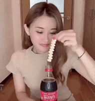 这是一个动态GIF图，画面中的女生起初低头，脸部被身前的饮料瓶完全遮挡，当她抬头时，脸部被AI特效替换成了一张精致的陌生脸庞，随后女生反应过来，立刻笑着用手捂住嘴巴，整个过程通过脸部的强烈反差制造出搞笑的效果。