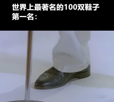 图片上半部分为黑色背景白色文字“世界上最著名的100双鞋子 第一名：”，下半部分是特写镜头，展示了一只穿着磨损黑色皮鞋的脚，搭配白色长裤，鞋头有明显的污渍和划痕，旁边有一根透明的杆子（疑似展示架）。整体通过“最著名鞋子第一名”的宏大标题与实际普通破旧皮鞋形成强烈反差，制造幽默调侃的效果。