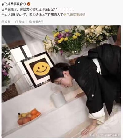 图片展示了一个悼念场景，一位身穿黑色正装的女性正在对着摆放有水果和鲜花的桌子鞠躬。背景中墙上挂着一个相框，里面却是一个黄色的笑脸表情包，而非传统的遗像照片。上方配有文字称日本传统文化被打压，未亡人题材片子的遗像不许用真人。