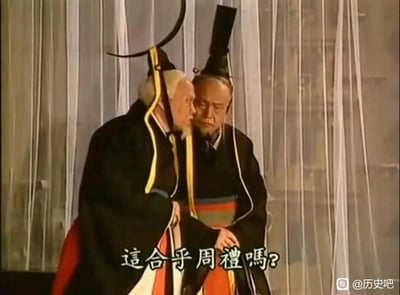 图片中两位身着古代官员服饰的老者正在进行严肃对话，其中一位侧身靠近另一位，似乎在低声询问或质疑。两人都头戴传统官帽，身穿黑色长袍配红色下摆。背景是白色幕布，营造出古代宫廷或朝堂的氛围。图片底部有文字"这合乎周礼吗？"，表达了对某种行为是否符合古代礼仪规范的质疑。