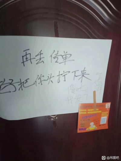 这是一张实拍的生活场景图，画面主体是住户的家门，门上用夹子固定着一张白纸，纸上用黑色笔写下愤怒的警告语“再丢传单 把你头拧下来”，还有被划掉的字迹，另外还有浅色手写的“傻比 我发了”的字样，显然是住户对被塞传单的不满宣泄。但讽刺的是，在白纸的旁边，依然被贴上了一张橙色的商业传单，形成了强烈的反差，展现出住户的警告并未起到作用，发传单者无视警告的我行我素，充满了无奈又搞笑的氛围。