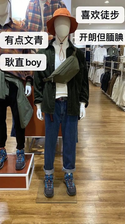 这张图片展示了一家服装店的男士模特，穿着带文艺气息的休闲装：橙色渔夫帽、白色T恤、深色开衫、牛仔裤和运动鞋，肩背斜挎包。画面配有多条标签，比如“有点文青”、“耿直boy”、“开朗但腼腆”、“喜欢徒步”。这些文字为模特植入了‘虚拟人设’，让一套普通穿搭带上了丰富的社交媒体性格想象，幽默调侃现实中这种服装风格的人常常被贴上的‘文青’、‘户外’、‘耿直’等标签，有一定网络趣味。整体语气轻松，略带自嘲。未见明显谐音梗、双关或暗示。