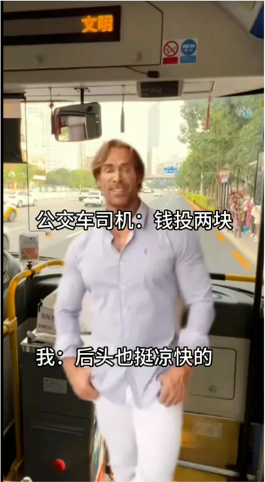 图片中美国健身网红迈克·奥赫恩以标志性的迷之自信表情站立在公交车内，背景可见车窗外的街道和树木。图中叠加了两组对话文本：公交车司机说“钱投两块”，而“我”却回应“后头也挺凉快的”，形成典型的“大力王文学”无逻辑对话，通过答非所问的方式讽刺盲目自信的行为，整体场景充满搞笑与荒诞感。