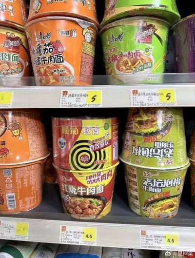 这是一张拍摄超市货架商品摆放的照片，货架上层正常摆放着康师傅桶装泡面，分别是番茄鸡蛋牛肉面和泡椒牛肉面，售价均为5元；下层补货摆放时出现了十分巧合的错误摆放：一罐榄菊蚊香被摆放在统一红烧牛肉丸泡面的上方，蚊香桶的尺寸和桶装泡面完全契合，刚好卡进货位，红黄色的包装也和周围泡面包装色调相近，违和感极低，搭配右侧倒置摆放的统一老坛泡椒牛肉面，这种出错了却意外和谐的巧合摆放十分搞笑，让人忍俊不禁。
