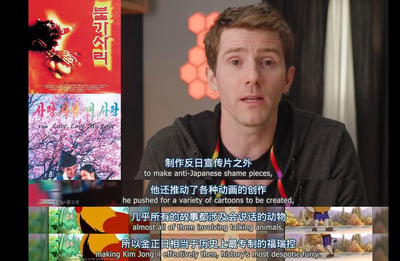 这是一段带有中英双语字幕的视频截图，画面右侧是一位表情惊讶的外国男性博主正在对着镜头讲述；画面左侧展示了两部朝鲜电影的海报，分别是怪兽电影《Pulgasari（불가사리，平壤怪兽）》和爱情电影《Love, Love, My Love（사랑 사랑 내 사랑）》，下方还有以会说话的动物为内容的动画截图。字幕内容调侃称，除了制作反日宣传片，还推动创作大量以会说话的动物为主题的动画，将金正日戏称为‘历史上最专制的福瑞控’，用网络热词玩梗，把严肃的影视创作话题用搞笑戏谑的方式呈现。