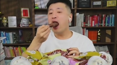 整张图的主体是网络知名博主张雪峰，他坐在摆满书籍、摆件的书架前，佩戴白色蓝牙耳机，身穿白色上衣，正将一支巧克力外皮的巧乐兹冰棍递到嘴边准备食用，他面前摆放着多包巧乐兹雪糕和多罐罐装饮料，这张图被用于“巧乐兹雪碧冰红茶三合一”的网络热梗创作，该梗结合了张雪峰与巧乐兹的关联、科比相关饮料谐音梗、张继科相关断句梗，属于黑色幽默类的组合玩梗内容。