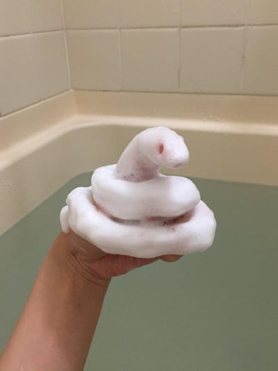 在浴室的浴缸旁，一只手被洁白的沐浴泡沫塑造成了盘绕的小蛇造型：泡沫层层包裹住手部，仅在上方留出模仿蛇头的形态，还做出了蛇的口鼻和眼睛的空洞，看起来栩栩如生，充满了即兴创作的趣味，是洗澡时玩出的生活小创意。
