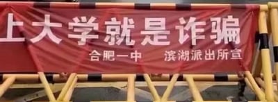 这是一张展示反诈宣传横幅的静态实拍图片，红色横幅被固定在黄黑相间的道路护栏上。横幅上方用醒目的大号白色字体写着“上大学就是诈骗”，下方用稍小的白色字体标注“合肥一中 滨湖派出所宣”。该标语采用夸张吸睛的表述方式，实际目的是提醒公众警惕虚假大学招生类的诈骗行为，通过反差感强烈的文字提升反诈宣传的关注度，避免群众落入“虚假上大学”的诈骗陷阱。