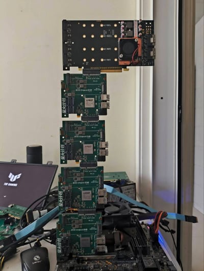 这是一张实拍的硬件调试工位照片，整体为竖版构图。画面核心位置是垂直串接堆叠的五块PCB板卡：最顶端是一块配备4个M.2接口、自带铜底散热风扇的PCIe扩展卡，下方依次插接了4块印有“星火计划”字样、搭载AMD B550芯片的EVB测试扩展板，所有板卡通过金手指PCIe接口依次连接。画面左侧可见印有华硕TUF GAMING标识的便携显示器、力胜品牌有线鼠标，桌面还散落着其他电路板、蓝色传输排线、各类线材，背景是浅色墙面与窗户边框，呈现出电子爱好者或硬件研发人员进行硬件改装、调试的工作场景。
