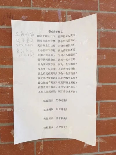 这是一张张贴在红砖墙上的竖版打印纸，主体是一篇名为《讨贼逆子檄文》的文言讨伐文，出自淮阴师范学院的一名外卖被盗学生之手。文章以文言格式撰写，先是描述自己取外卖时发现骑手已离开，自己焦急寻找却遍寻不见的过程，随后将矛头指向偷外卖的同校学生，从指责对方身为同窗却因一口吃食失德，到用激烈的语句辱骂对方家人，层层递进地宣泄自己的愤怒。在纸张左侧还有手写的补充内容：“没钱吃饭 跟你爹说”、手机号“18835382686”以及“爹给你买 好吗！”，用带着嘲讽的语气进一步表达自己的不满，整体内容将失主的愤怒、无奈又带着嘲讽的情绪展现得淋漓尽致。