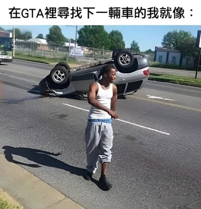 图片上方配有文字“在GTA裡尋找下一輛車的我就像：”，下方是一张实拍照片：一名穿着白色背心和灰色运动裤的黑人男子站在马路中央，身旁是一辆四轮朝天的灰色轿车，车辆疑似发生事故侧翻，路面上有油渍痕迹。男子表情显得有些漠然，肢体动作随意，仿佛对眼前的翻车场景习以为常。这张图通过现实中的汽车侧翻场景与GTA游戏中玩家频繁需要更换车辆（因原车辆损坏或被摧毁）的体验相结合，形成幽默对比，调侃玩家在游戏中找车时的无奈与“淡定”。