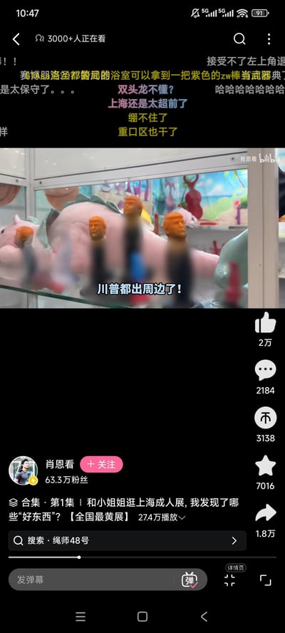 Bilibili视频截图展示上海成人展现场，画面中央为玻璃展示柜，内有粉色造型物品及多个橙色头部的川普（特朗普）造型周边摆件。视频标题为《和小姐姐逛上海成人展，我发现了哪些好东西？【全国最黄展】》，上传者“肖恩看”拥有63.3万粉丝，播放量达274万。屏幕上方覆盖大量实时弹幕，网友评论“川普都出周边了！”“上海还是太超前了”“接受不了左上角这”“绷不住了”等，反映对展品的惊讶与调侃。界面显示3000+人正在观看，互动数据包括点赞2万、评论2184条、收藏7016次、分享1.8万次。图中无明显双关或谐音梗，主要为展会现场记录与观众实时互动场景。