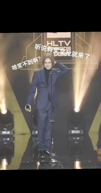 这是一张网友制作的调侃梗图，主体是CS2职业选手donk在HLTV颁奖典礼的领奖现场画面，他穿着深蓝色西装套装，站在舞台麦克风前，一只手拿着奖杯，另一只手摸着后脑勺，面带笑意，画面上添加了白色文字“听说有奖拿我就来了”“啥奖不到啊？”，调侃donk实力强劲、在赛事中表现突出，获奖众多的情况。