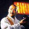 图片中是一位身着白色传统风格上衣的男子，他右手手持一个黑色物品，背景呈现温暖的黄色调，整体画面类似人物肖像，氛围平和，未发现明显的文字信息或双关、谐音梗等元素。