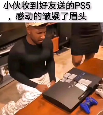 这张图展示了一个男生坐在桌前，面前是一台被合成的“PS5”主机，其实是两台PS2游戏机叠在一起，并用胶带拼成了“PS5”的字样。图片顶部配有搞笑文字，称“小伙收到好友送的PS5，感动的皱紧了眉头”，制造了强烈的反差和幽默效果。

图片双关/梗点在于：用两个PS2（PlayStation 2）组合假装是PS5（PlayStation 5），通过拼贴和胶带把PS2字母拼成PS5，黑色幽默很强。这是一种常见的“穷人式DIY幽默”。