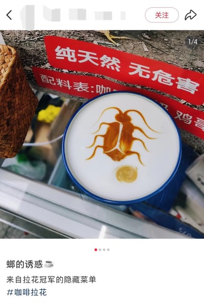 图片展示了一杯蓝色咖啡杯中的拿铁，奶泡上用焦糖酱绘制了一只蟑螂形象的拉花，其超长触角形似“广式双马尾”梗中的标志性特征。背景可见红色标语牌，上面写有“纯天然 无危害”和“配料表:咖...”等字样。图片下方配有文字“螂的诱惑☕ 来自拉花冠军的隐藏菜单 #咖啡拉花”。该图通过将网络热梗“广式双马尾”（广东地区美洲大蠊的戏称）与咖啡拉花结合，形成反差萌的幽默效果，体现了网民用趣味方式解构生活现象的创意。