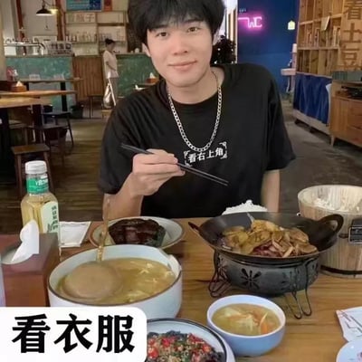 一名男子坐在餐厅餐桌前，桌上摆放着红烧肉、火锅、汤等多道菜肴，左手边有一瓶农夫山泉。他穿着黑色T恤，T恤上印有白色文字“看右上角”，手中拿着筷子，面带微笑准备用餐。图片底部有文字“看衣服”提示关注T恤内容。背景可见餐厅内的其他顾客、木质桌椅和霓虹灯牌，整体氛围轻松愉悦。