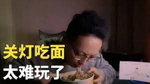 图片中一名人物在昏暗环境下低头专注地吃着面条，画面左侧有醒目的黄色大字叠加文字“关灯吃面 太难玩了”。整体场景通过昏暗的光线和人物低头吃面的动作，直观呈现出“关灯吃面”这一经典网络梗所蕴含的失意与无奈情绪，文字“太难玩了”则进一步强化了对某事感到挫败的表达。