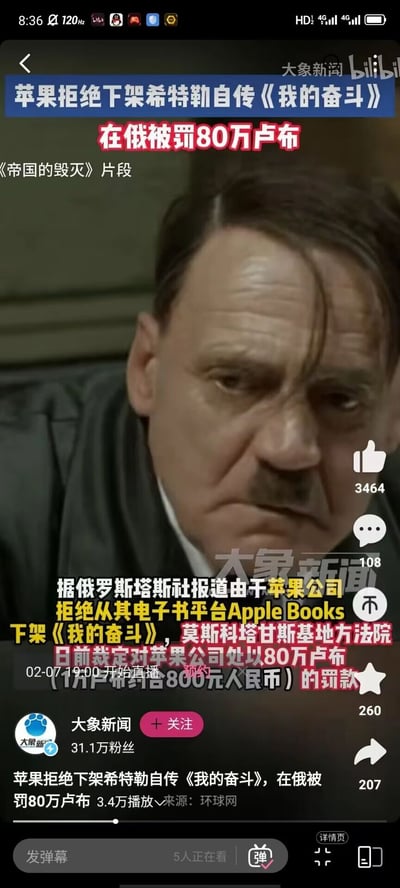 这是bilibili平台上大象新闻发布的新闻视频截图，视频采用电影《帝国的毁灭》中希特勒的面部特写片段作为画面素材，新闻核心内容为苹果公司拒绝从其电子书平台Apple Books下架希特勒自传《我的奋斗》，被莫斯科塔甘斯基基地方法院裁定处以80万卢布（约合8000元人民币）的罚款。截图中显示了新闻的相关文字说明，还包含视频的互动数据：点赞3464、评论108、收藏260、转发207，同时标注了02-07 19:00的直播预约信息。