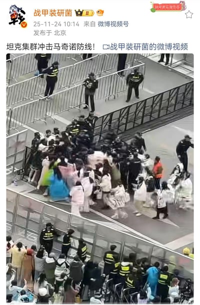 这是微博用户「战甲装研菌」发布的现场视频截图，画面中大量粉丝冲破现场的金属护栏，安保人员在周围维持秩序。博主用「坦克集群冲击马奇诺防线」的军事梗来调侃粉丝的狂热行为，将冲栏的粉丝比作冲击防线的坦克集群，安保与护栏比作马奇诺防线，用夸张的军事比喻放大了现场的混乱与粉丝的狂热氛围。