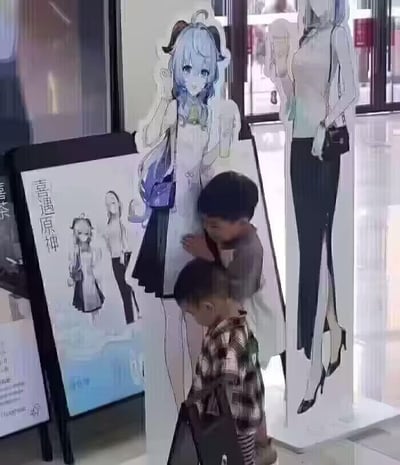 照片中展示了两个小朋友正在与商场内的原神角色立牌互动。一个小男孩正仰头看着蓝色头发的动漫角色立牌，另一个孩子则在旁边。立牌上的角色有着蓝色长发、角状装饰和紫色的包，穿着白色上衣和深色短裙。背景中可以看到另一个穿着职业装的女性角色立牌。左侧展板上有'喜遇原神'的字样和角色设计草图，显示这可能是原神主题的商业活动或联名展览。整个场景发生在明亮的室内商业空间，可能是购物中心或专卖店内。