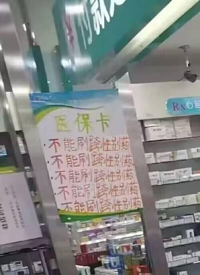 这是一张在实体药店内拍摄的静态图片，画面主体是一张张贴在金属立柱上的手写告示，告示顶部用黄色字体写着“医保卡”，下方用红色字体重复五次“不能刷跨性别药”，以此明确医保卡的使用限制。背景中可以看到药店的货架，上面摆放着各类药品，上方还有绿色的付款区域标识，整体场景清晰，是药店为了规范医保卡使用、告知顾客医保刷卡范围而设置的提示，图中没有双关、谐音梗或暗示内容。