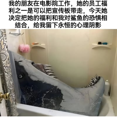 图片上方是一段文字说明，讲述朋友利用电影院工作的员工福利带走鲨鱼宣传板，结合自己对鲨鱼的恐惧进行恶作剧。下方照片展示了一个逼真的鲨鱼头宣传板被放置在浴缸中，鲨鱼嘴巴大张露出锋利牙齿，从浴缸中