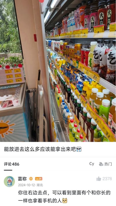 这是一张社交媒体帖子截图，拍摄内容为便利店的冷藏饮料展示柜，柜子内部从最内侧到开口处被各类瓶装、罐装饮料完全填满，几乎没有多余空隙。发帖人配文提问“能放进去这么多应该能拿出来吧😎”，下方一条高赞热门评论调侃回复，指出拍摄者正站在两个冰柜之间的狭窄缝隙中，对面冰柜的镜面能看到拿着手机拍照的拍摄者本人，实际上根本没办法伸手进去取出放在内侧的饮料，刚好印证了这张图原本“手伸不进去”的猜测。