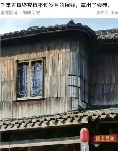 这是一张拍摄于湖南的古镇木质老建筑照片，建筑有着传统的青瓦片屋顶，墙面是风化的木质板材，窗户分为两种：一种是带有圆形铁艺装饰的玻璃窗，另一种是方格玻璃窗，下方悬挂着红灯笼，还有“楼上包厢”的招牌，充满古镇烟火气。
配文“千年古镇终究抵不过岁月的摧残，露出了瓷砖”是玩谐音梗：将窗户上的圆形铁艺玻璃调侃为“瓷（磁）砖（砖）”，用文字制造反差搞笑效果，把建筑的老旧感转化为趣味笑点。