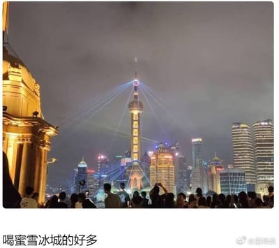这是一张经过创意改编的上海外滩夜景静态照片，画面中上海地标东方明珠广播电视塔的灯光效果，因视觉巧合和可能的P图调整，与蜜雪冰城的品牌标志高度相似。下方聚集的大量举着手机拍照的游客，被配文“喝蜜雪冰城的好多”调侃成排队购买奶茶的人群，制造出一种地标建筑变成蜜雪冰城门店、众人扎堆买奶茶的荒诞搞笑错觉，利用视觉相似性打造出接地气的场景梗。