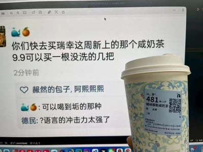 这张图片为实拍内容，右侧是一只手拿着的瑞幸新品锡林郭勒咸奶茶杯，杯身标签标注了该饮品为热饮、大杯、少甜，还有取餐号、二维码等信息；左侧背景是电脑屏幕显示的社交平台动态内容，发布者头像是鲸鱼和橘子的emoji，首先发文推荐瑞幸本周新上的咸奶茶，随后玩谐音梗称“9.9可以买一根没洗的几把”，还自行回复补充“可以喝到垢的那种”，另有其他用户“德民”评论表示“?语言的冲击力太强了”，该内容是利用“锡林郭勒”的读音谐音创作的搞笑梗。